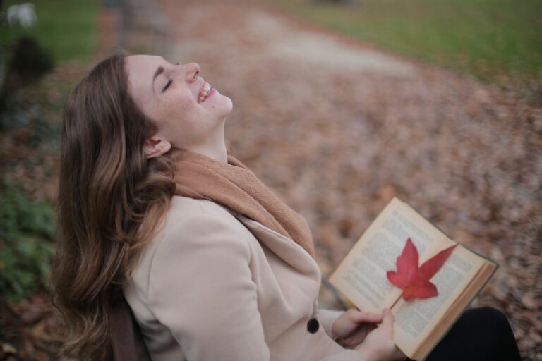 cheerful young woman with red leaf enjoying life and weather while reading book in autumn park. National Limerick Day