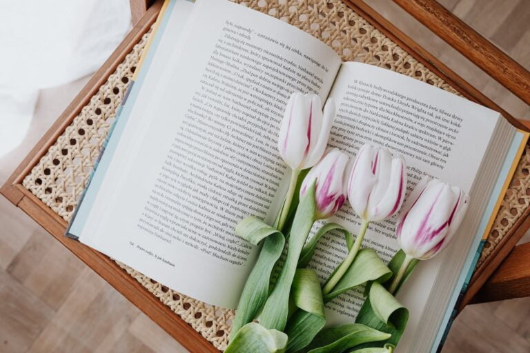 composition of fresh romantic flowers on open book arranged on vintage wicker table at home. Best books in April