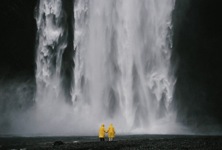 anonymous travelers holding hands against spectacular waterfall, appreciating nature