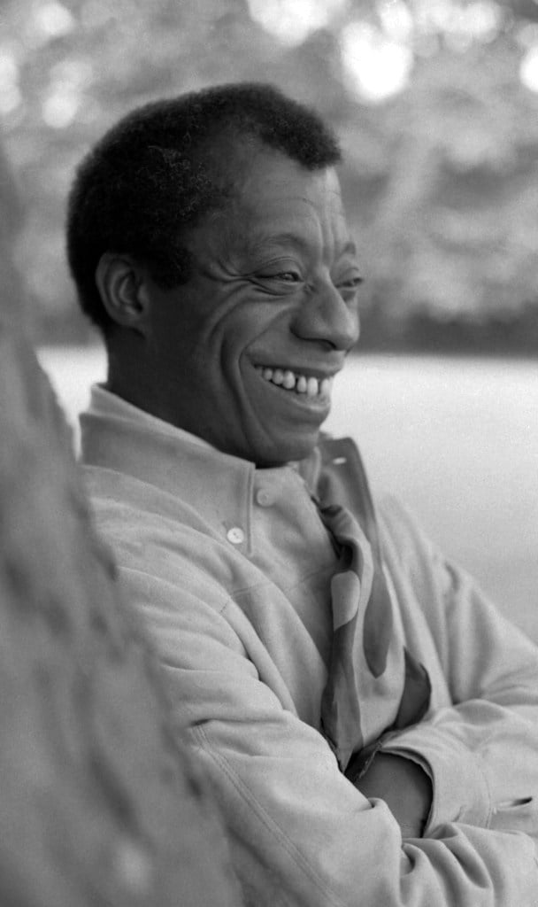 Black and white image of James Baldwin, leaning against a tree and laughing as Google Doodle celebrates his life. Taken in Hyde Park London.