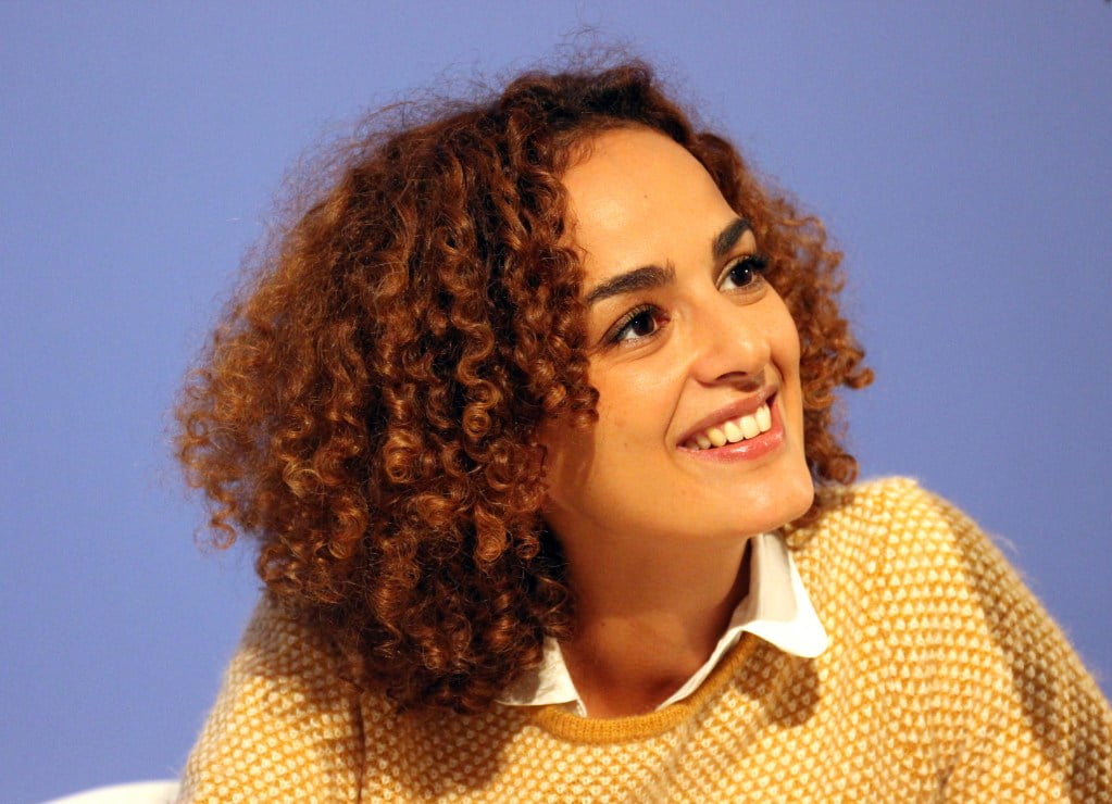 Leila Slimani in  yellow jumper and white shirt against a blue background