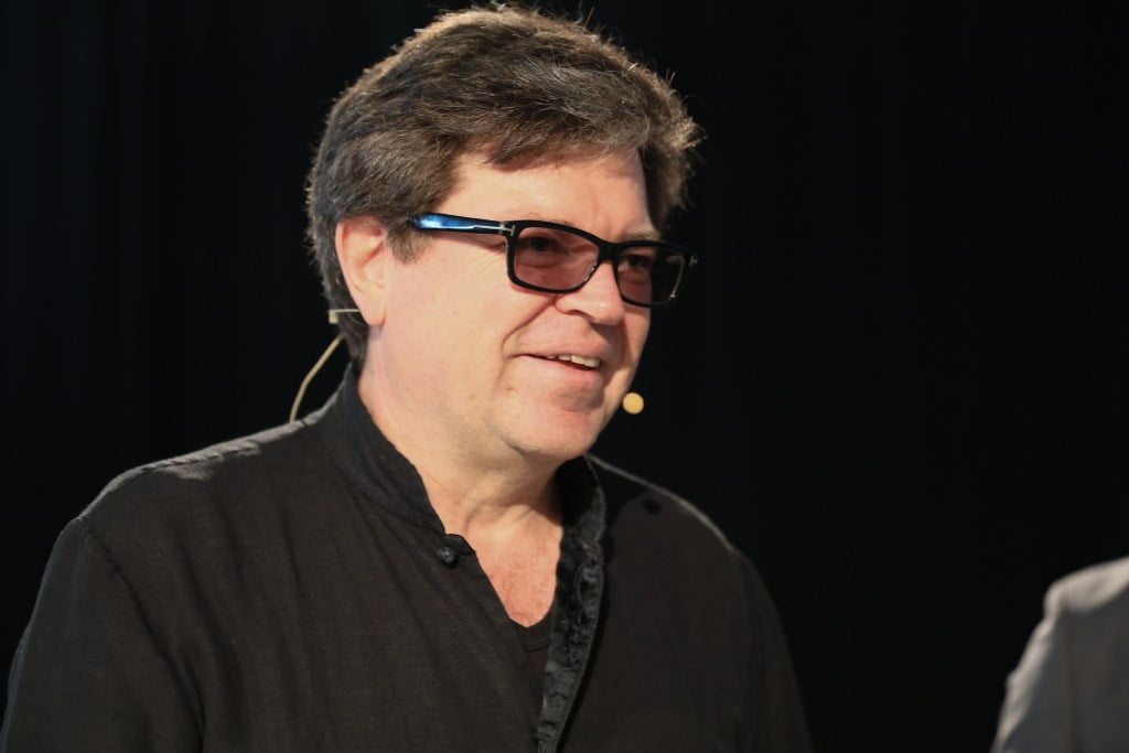 Yann Lecun, chief AI scientist of Meta, under fire over suggesting authors should give away books for free. He is wearing a black shirt and has dark glasses, standing in front of a black background.