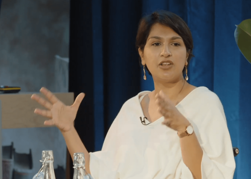 Angela Saini speaking animatedly at HistFest 2024, with a large screen behind her.