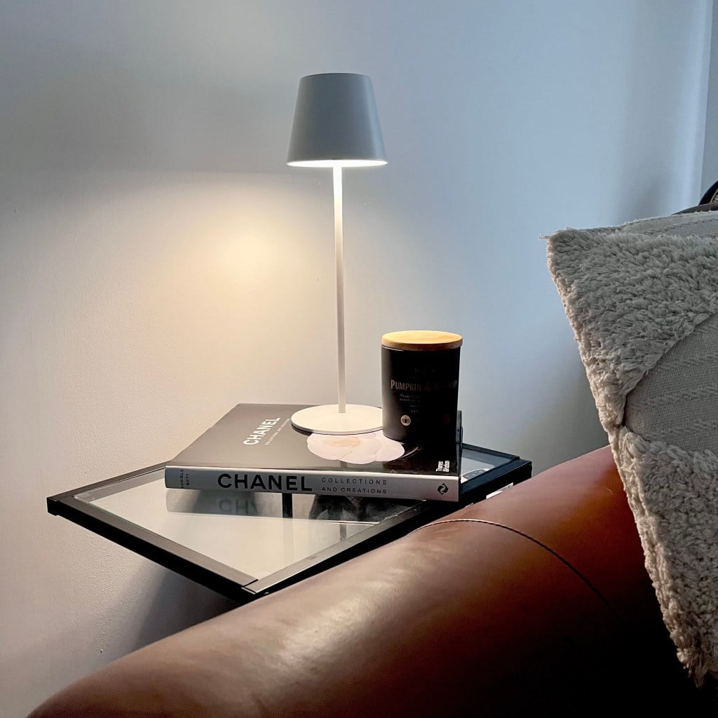 Chanel book under a lampshade and candle on a side table, showcasing bookshelf wealth.